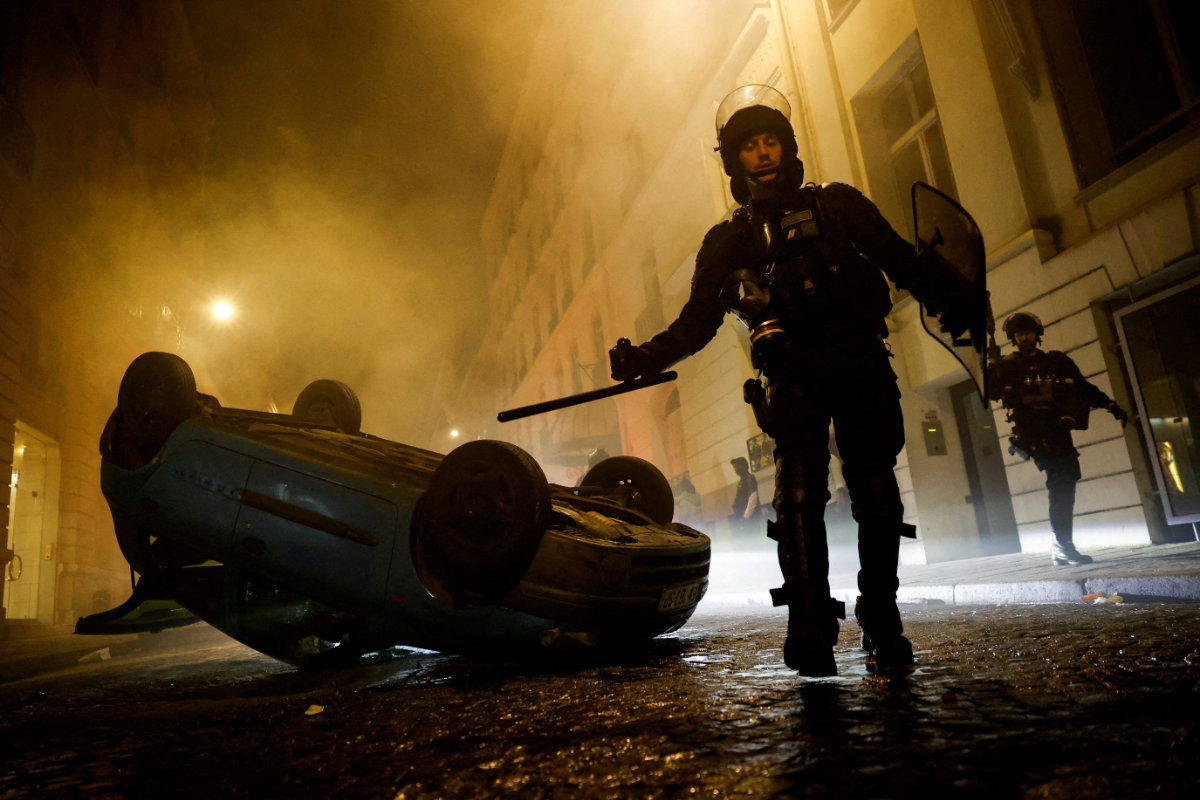 French riot police officers walk next to a vehicle upside down during protests in Paris on July 2, 2023. The riots were sparked by the death of Nahel, a 17-year-old teenager who was shot by a police officer during a traffic stop in Nanterre. (REUTERS/File Photo)