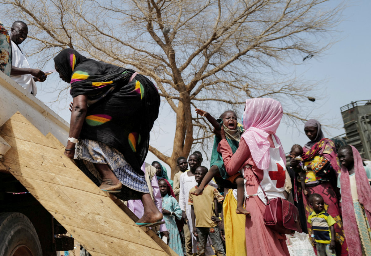 A Red Cross worker holds a child while his mother, a Sudanese woman who fled the conflict in Geneina in Sudan's Darfur region, climbs on a truck that will relocate them from a school where they were temporarily accommodated to a refugee camp, in Adre, Chad July 23, 2023. (REUTERS)