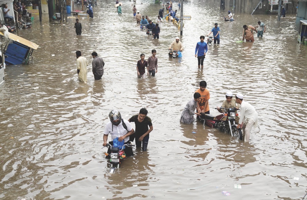 Motorcyclists drive and people wade through a flooded roadway caused by heavy monsoon rainfall in Lahore, Pakistan, Wednesday. (AP)