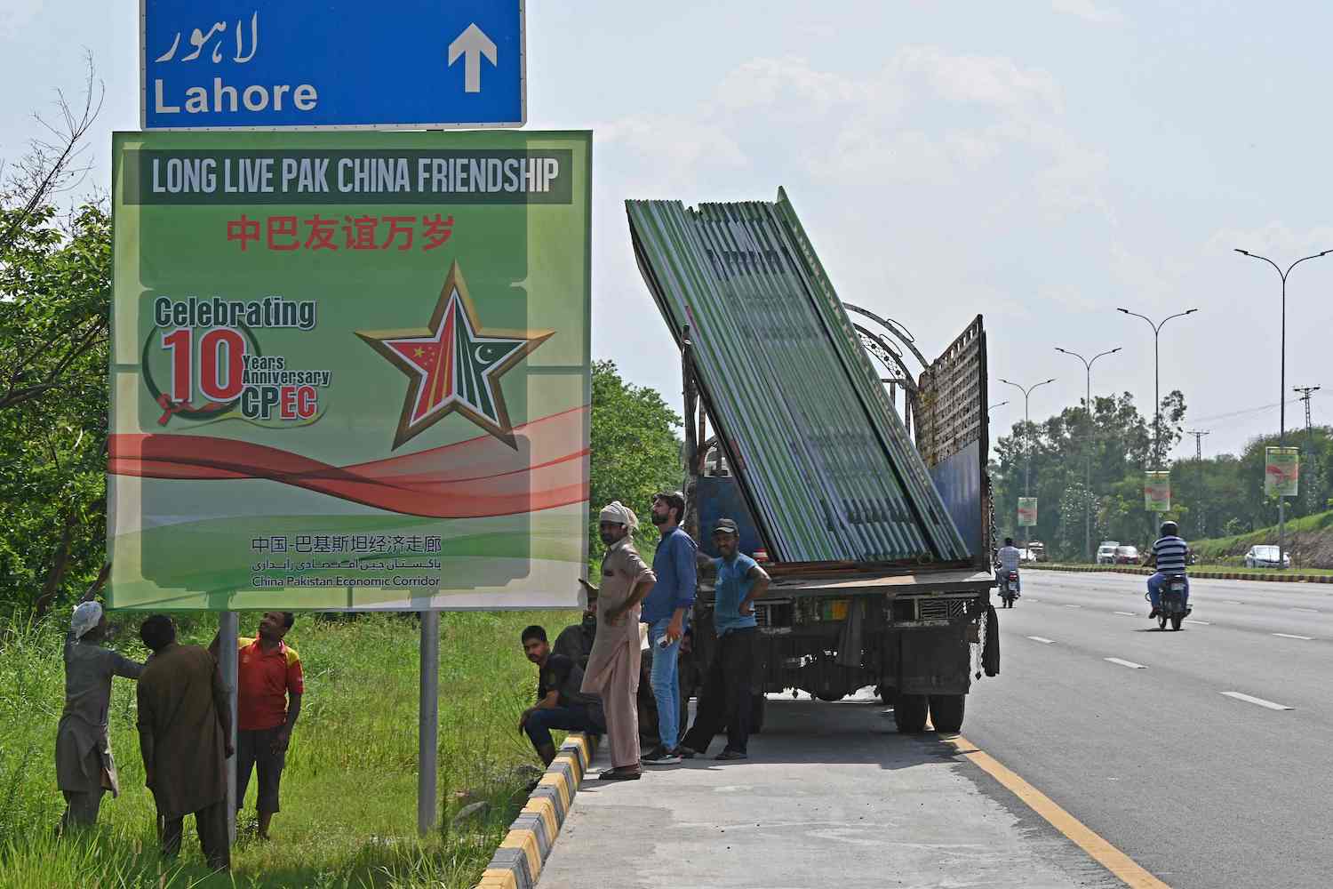 Workers install billboards along a roadside ahead of the visit of Chinese Vice Premier He Lifeng, in Islamabad on July 30, 2023. (AFP)