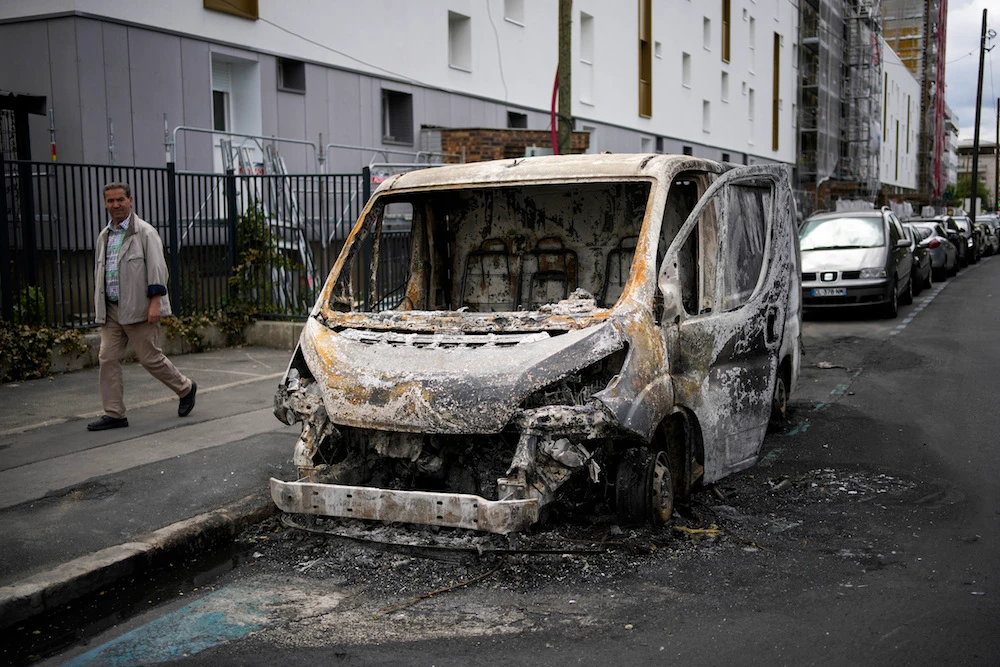 A man walks past a burned van on the aftermath of protests in Colombes, outside Paris, Saturday, July 1, 2023. The fatal shooting of Nahel, whose last name has not been made public, stirred up long-simmering tensions between police and young people in housing projects who struggle with poverty, unemployment and racial discrimination. (AP)