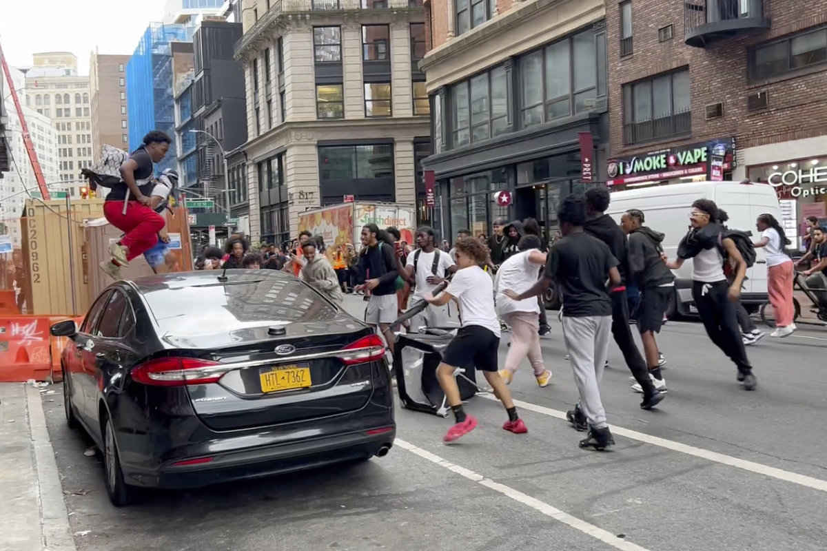 In this photo taken from video, a man jumps on a car as a crowd runs through the street on Broadway near Union Square on Friday in New York. (AP)