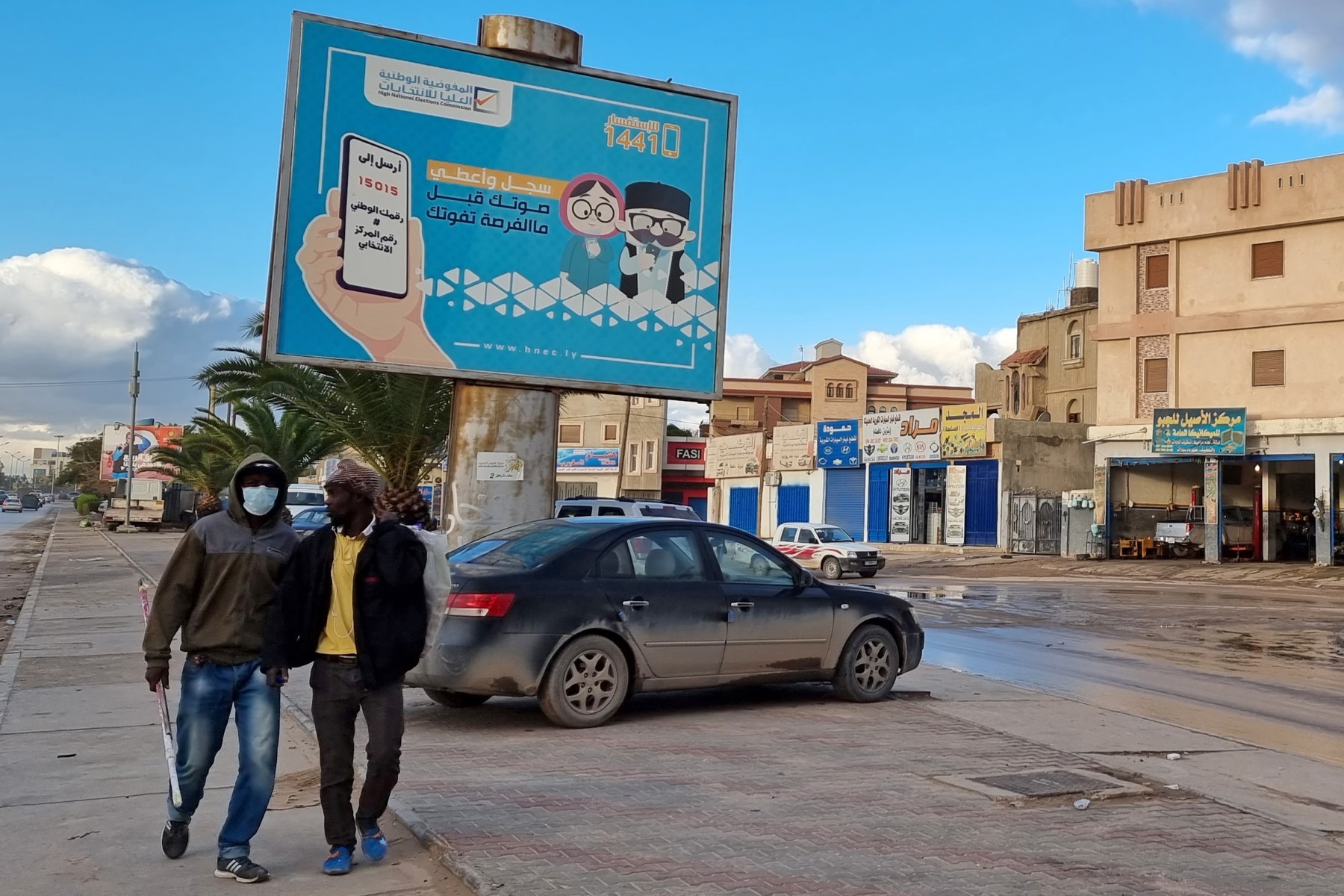 Workers walk by an electoral billboard reading in Arabic "register and vote before missing your chance" in Libya's capital Tripoli on December 14, 2021. (AFP)