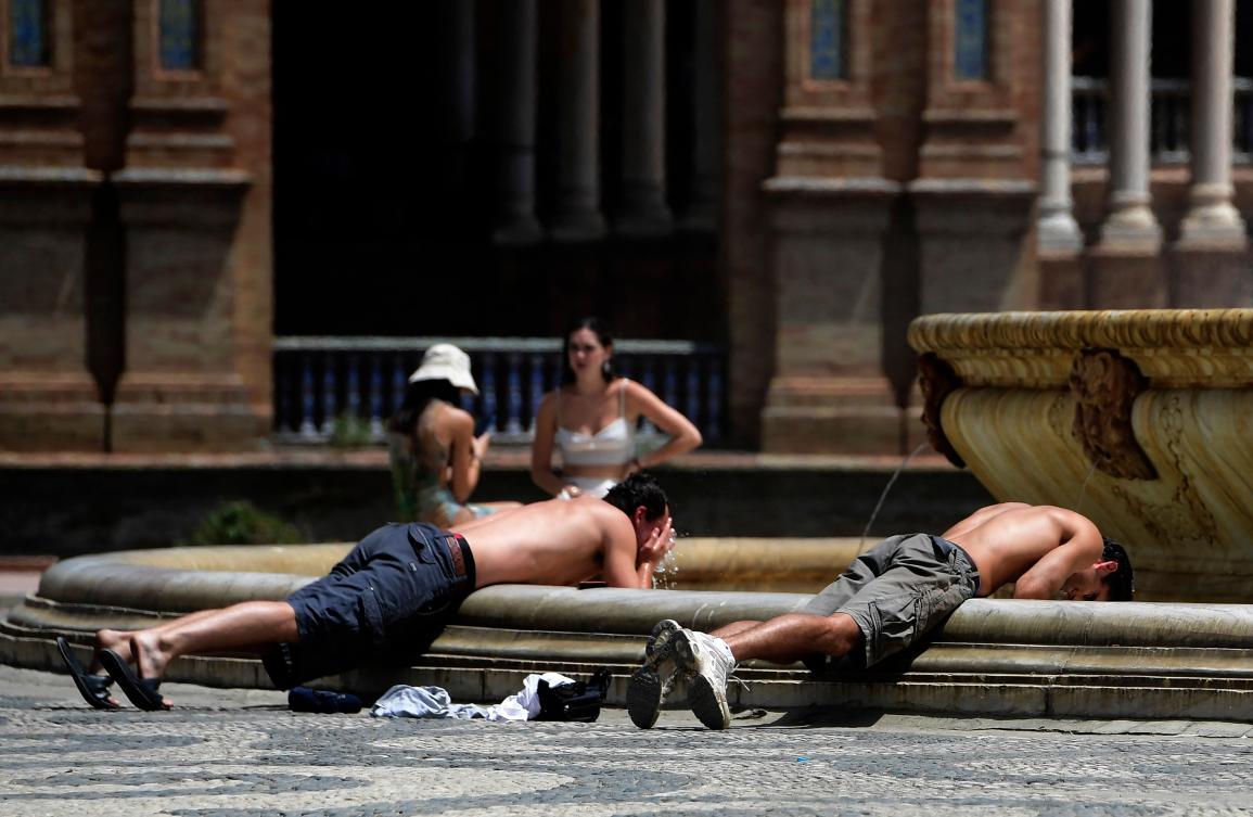 Two youths plunge their heads into the water of a fountain to cool off, in Plaza de Espana square in Seville on August 7, 2023. (AFP)