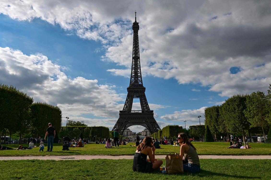 Tourists and Parisians sit in the Champ de Mars in front of the Eiffel Tower in Paris on August 9, 2023. (AFP)