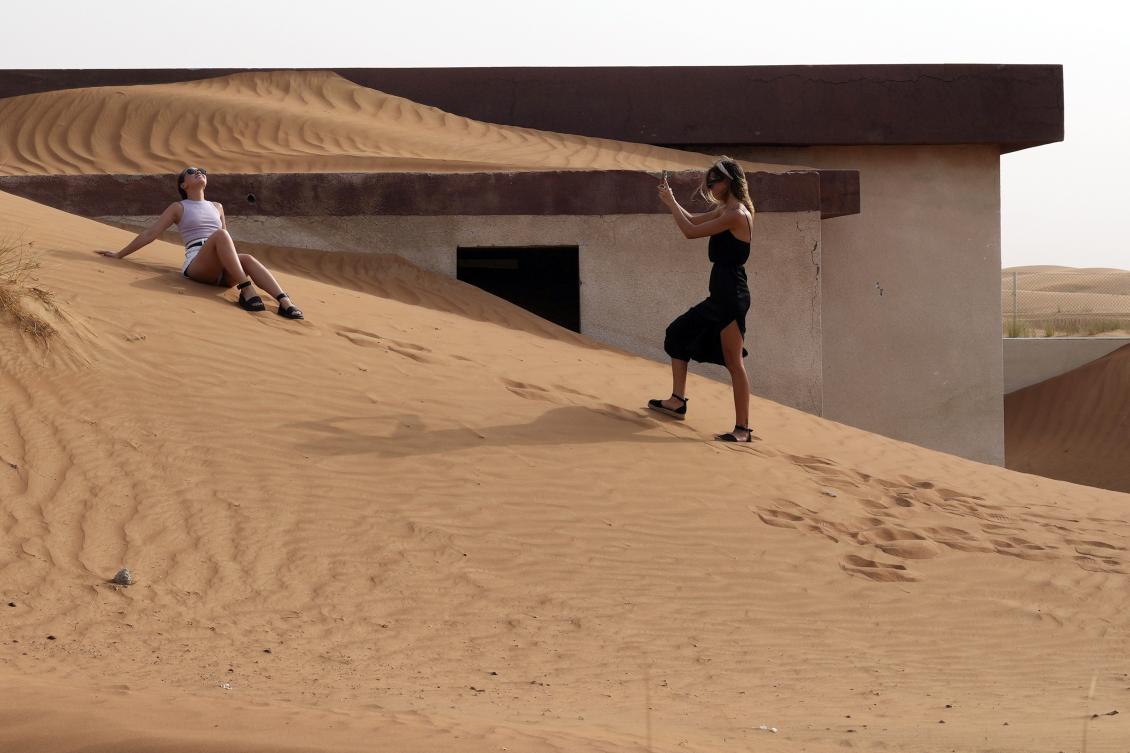 A woman poses for a photo in front of a house buried under the sand at the Bedouin village of al-Ghuraifabout 100 km, 62 miles, southeast of Sharjah, United Arab Emirates (AP)