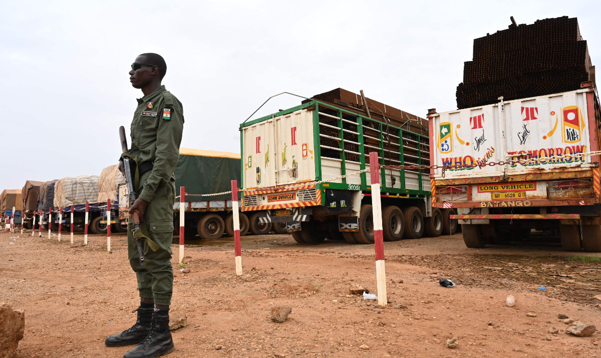 A Niger’s police officer stands guard next to some of the 300 trucks mainly loaded with food that arrived from Burkina Faso in Niamey on August 21, 2023. (AFP)