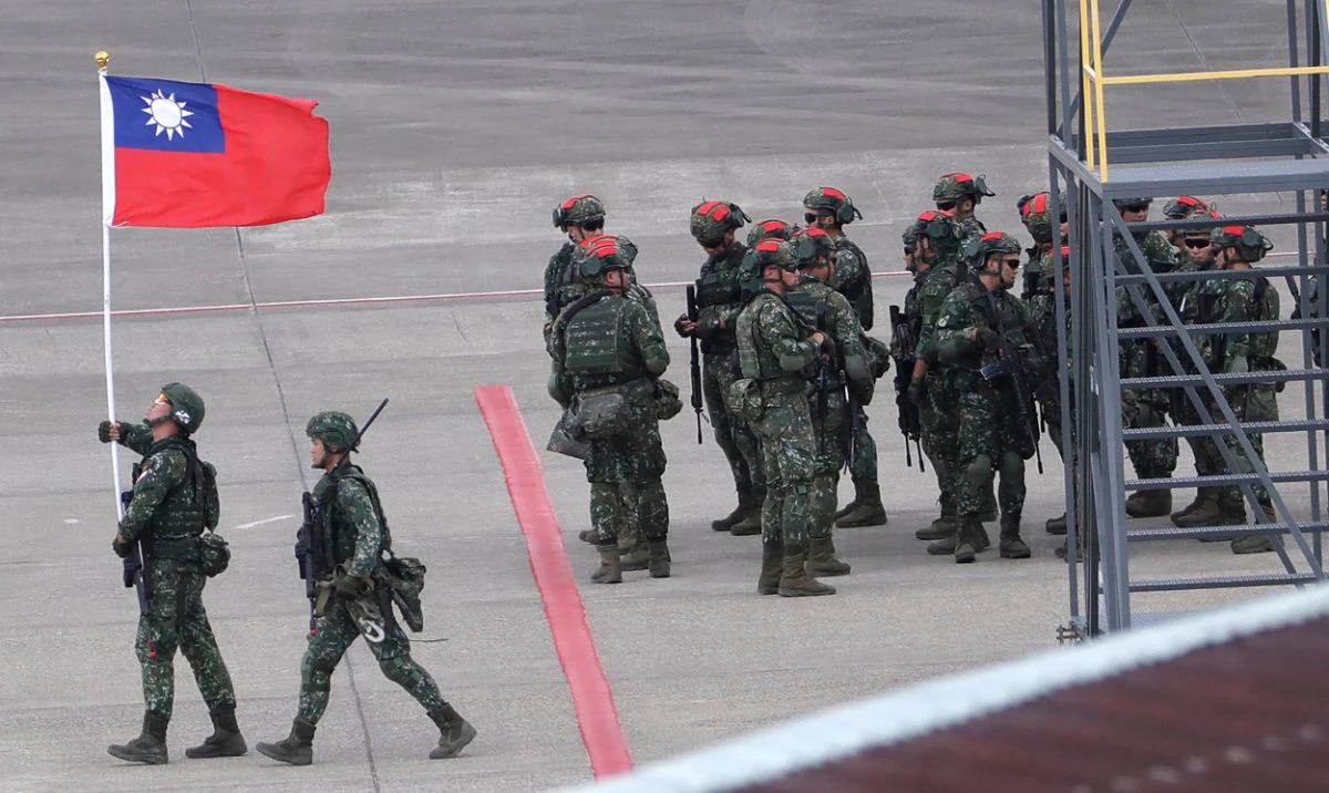 A Taiwanese soldier holds a Taiwan national flag near a group of soldiers with red markings on their helmets to play the role of an enemy during the annual Han Kuang military exercises simulating an attack on an airfield at Taoyuan International Airport in Taoyuan, Northern Taiwan, July 26, 2023. (AP)