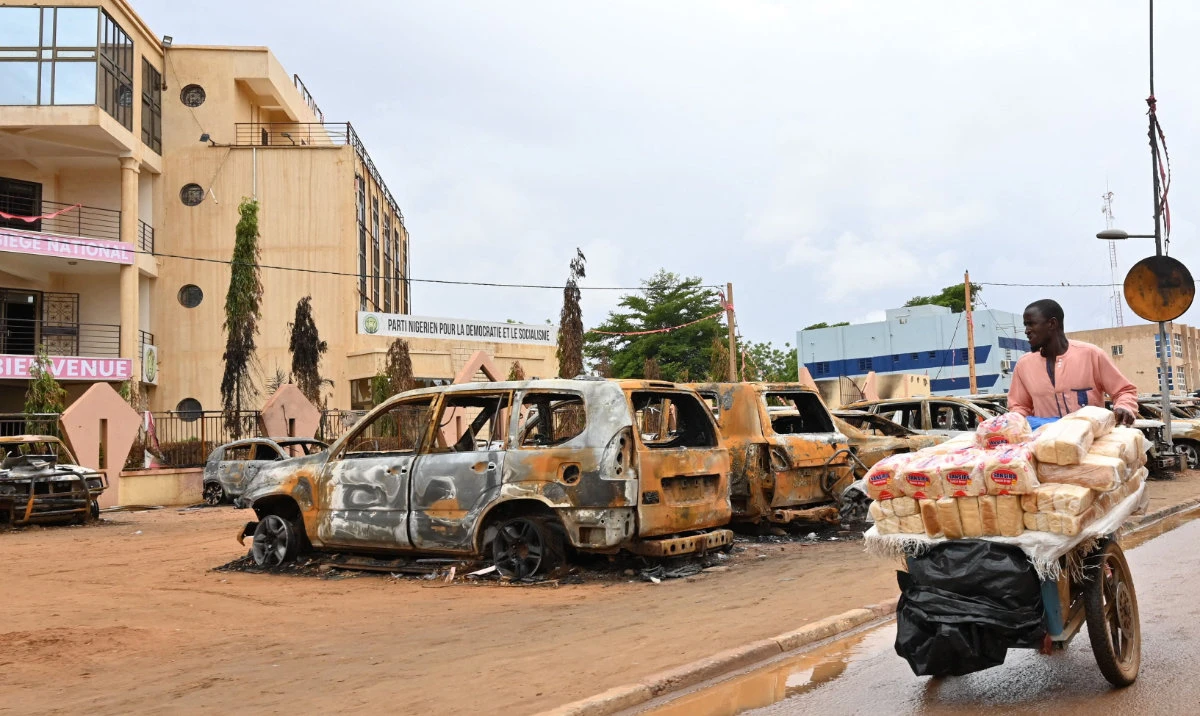 A street vendor pushes his cart past burned cars outside the headquarters of president Bazoum’s Nigerien Party for Democracy and Socialism in Niamey on August 7, 2023. (AFP)