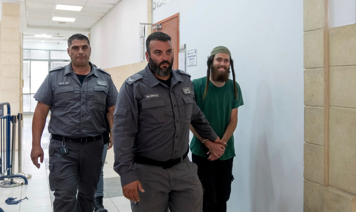 Elisha Yared, 22, right, is led handcuffed by officers during an appearance at the Jerusalem District Court on Tuesday, Aug. 8, 2023. Yared is one of two Israeli settlers arrested on suspicion of involvement in the killing of a Palestinian man in the West Bank on Friday. (AP)