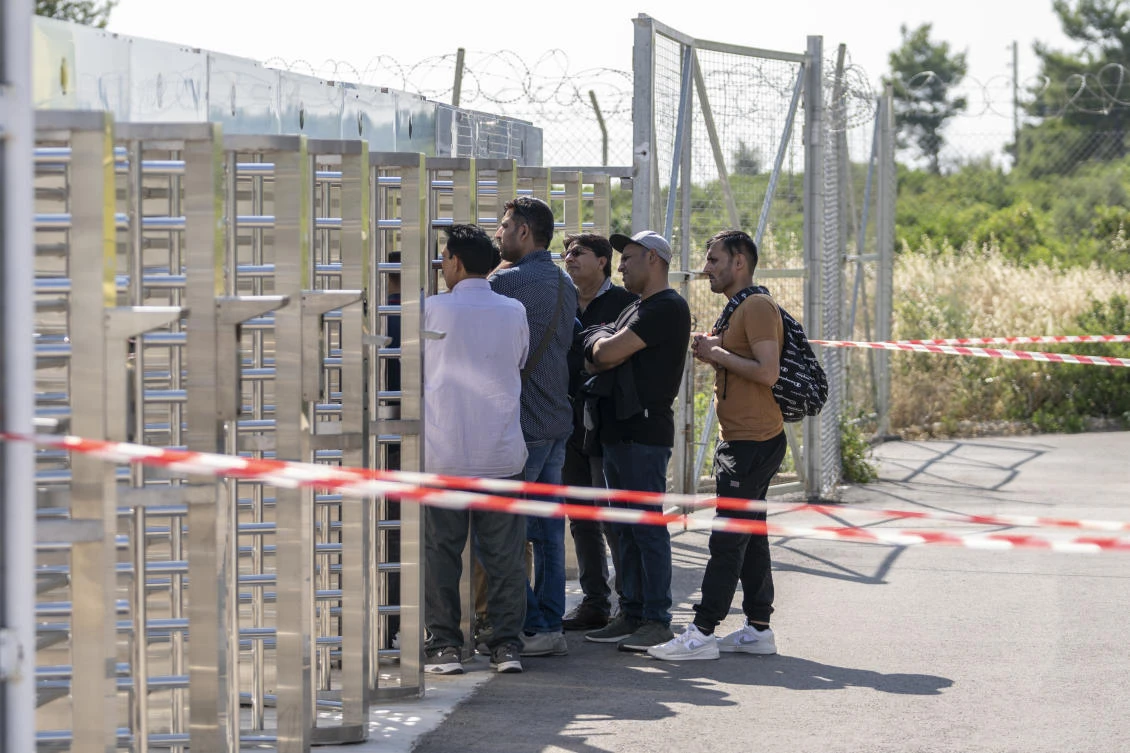 A group of men wait at the turnstiles and speak with survivors, mostly from Pakistan, of a deadly migrant boat sinking at a migrant camp in Malakasa north of Athens. (File/AP)
