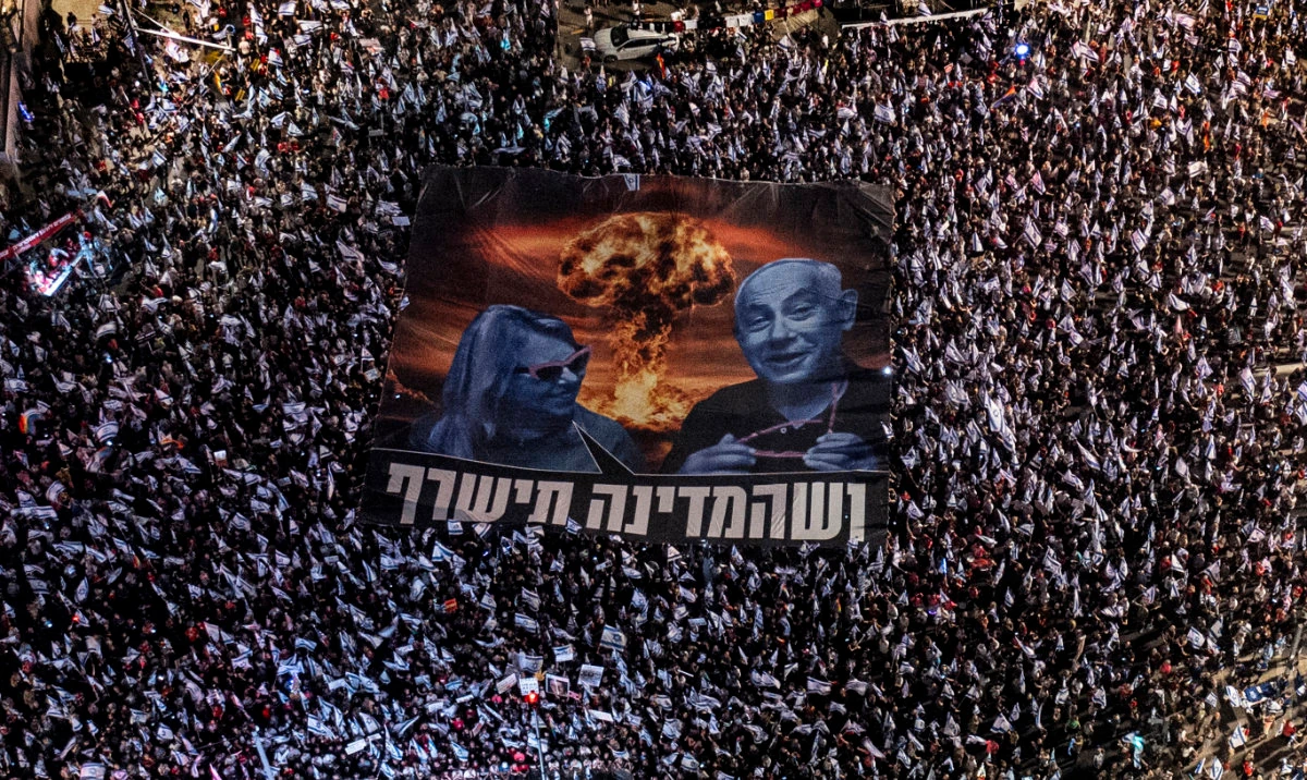 Israelis gather for the 34th consecutive week to protest against plans by Prime Minister Benjamin Netanyahu's government to overhaul the judicial system, in Tel Aviv, Aug. 26, 2023. The large banner depicts Netanyahu and his wife, Sara, with Hebrew that reads: "let the country burn." (AP)