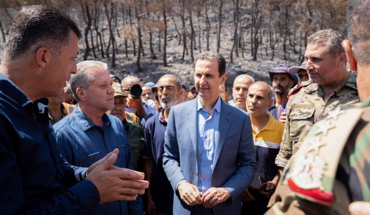 President Bashar Al-Assad (C) speaking with fire fighters and emergency responders at the site of a forest fire in the countryside of the northwestern Latakia province. (AFP)