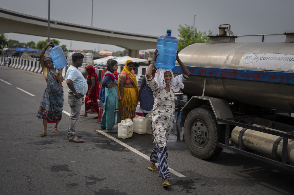 Rekha Devi carries drinking water from a municipality water tanker to her temporary shelter on an under construction overpass after her family evacuated the flooded banks of the Yamuna River in New Delhi, India, on Aug. 9, 2023. (AP Photo)