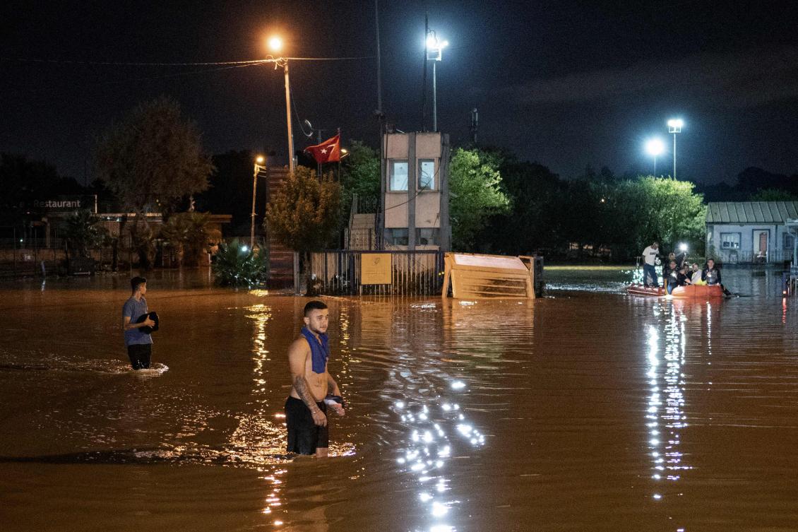 People stand in a flooded street while other are evacuated by boat in Kucukcekmece district in Istanbul (AFP)