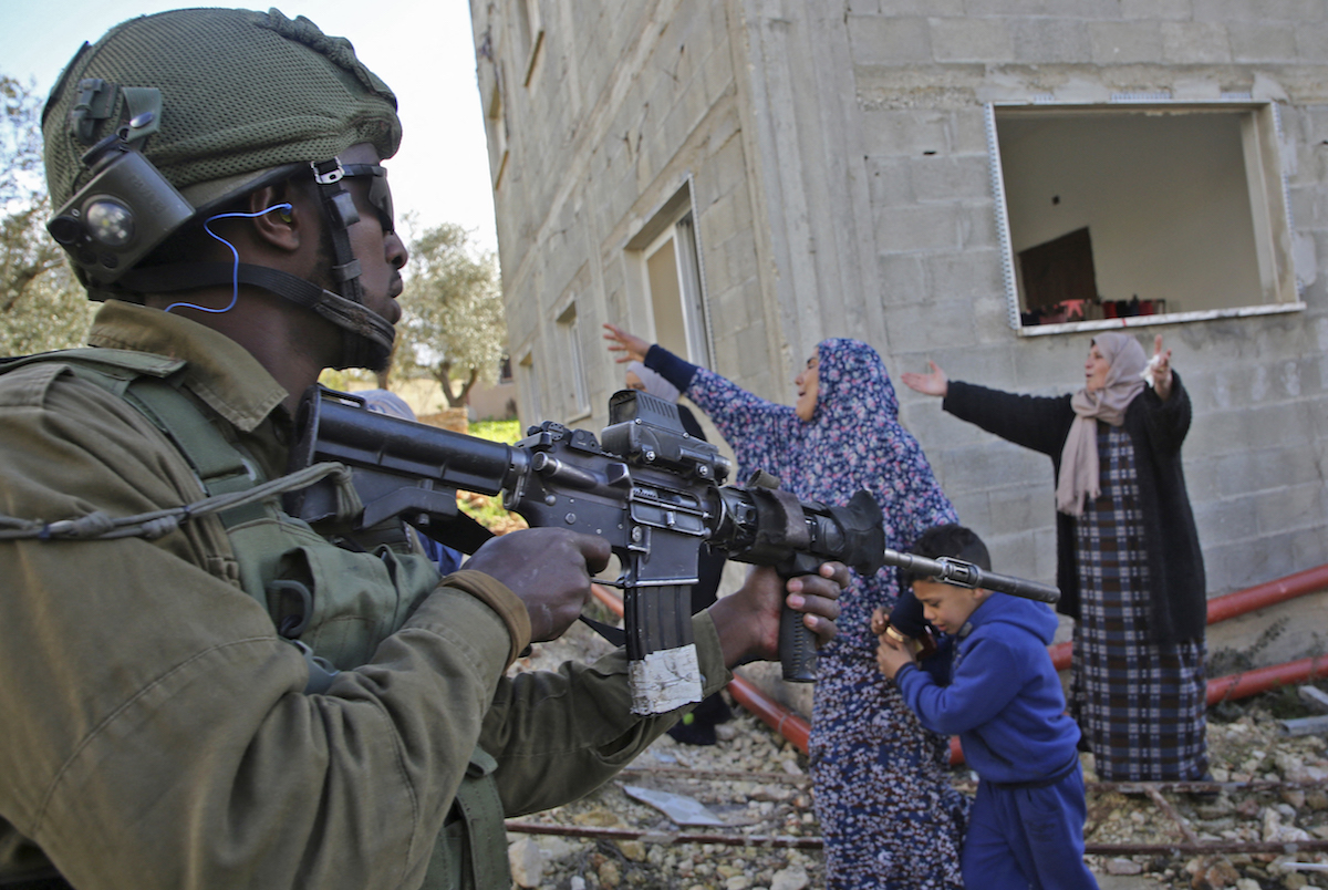 An Israeli soldier stands guard holding an assault rifle as Palestinian women protest. (File/AFP)