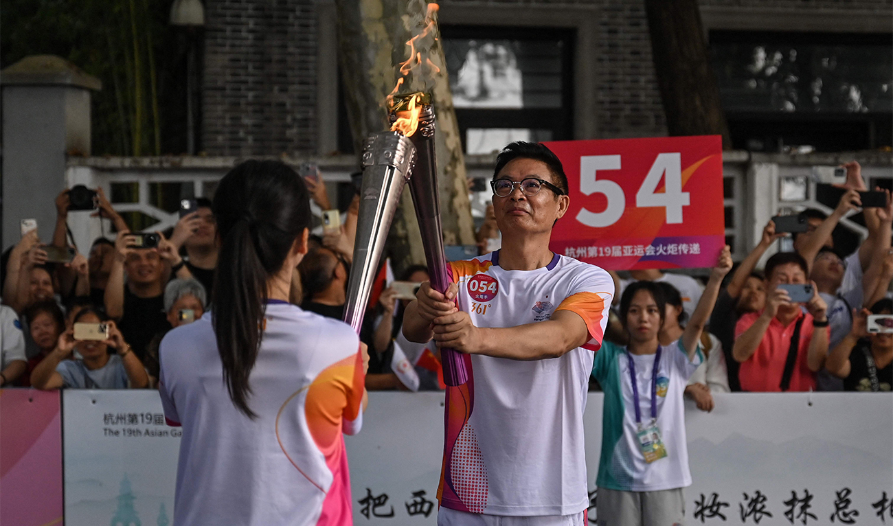 Jiaxing Ye (L), a traditional Chinese ceramist, and writer Mai Jia exchange the flame during the Asian Games torch relay in Hangzhou, China, on September 8, 2023. (Photo courtesy: AFP)