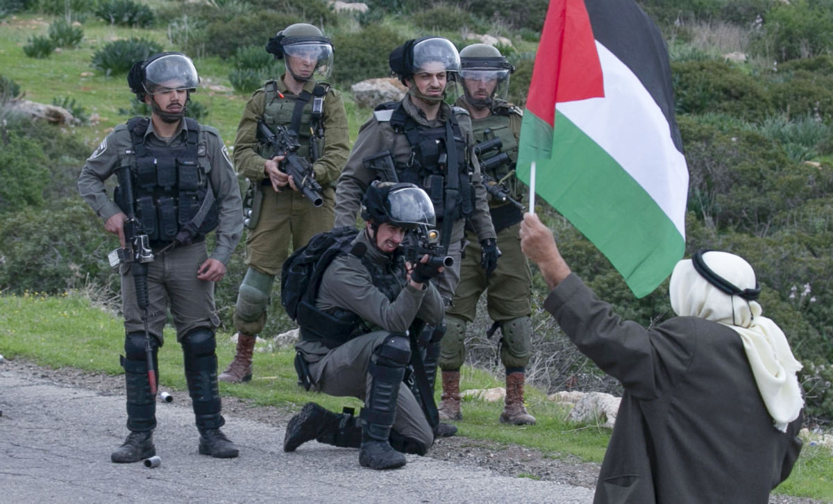 A man brandishes a Palestinian flag as members of the Israeli border police clash with Palestinians protesting Israeli settlements and a controversial US-brokered peace plan, in the Jordan Valley area of the occupied West Bank, on February 25, 2020. (AFP)