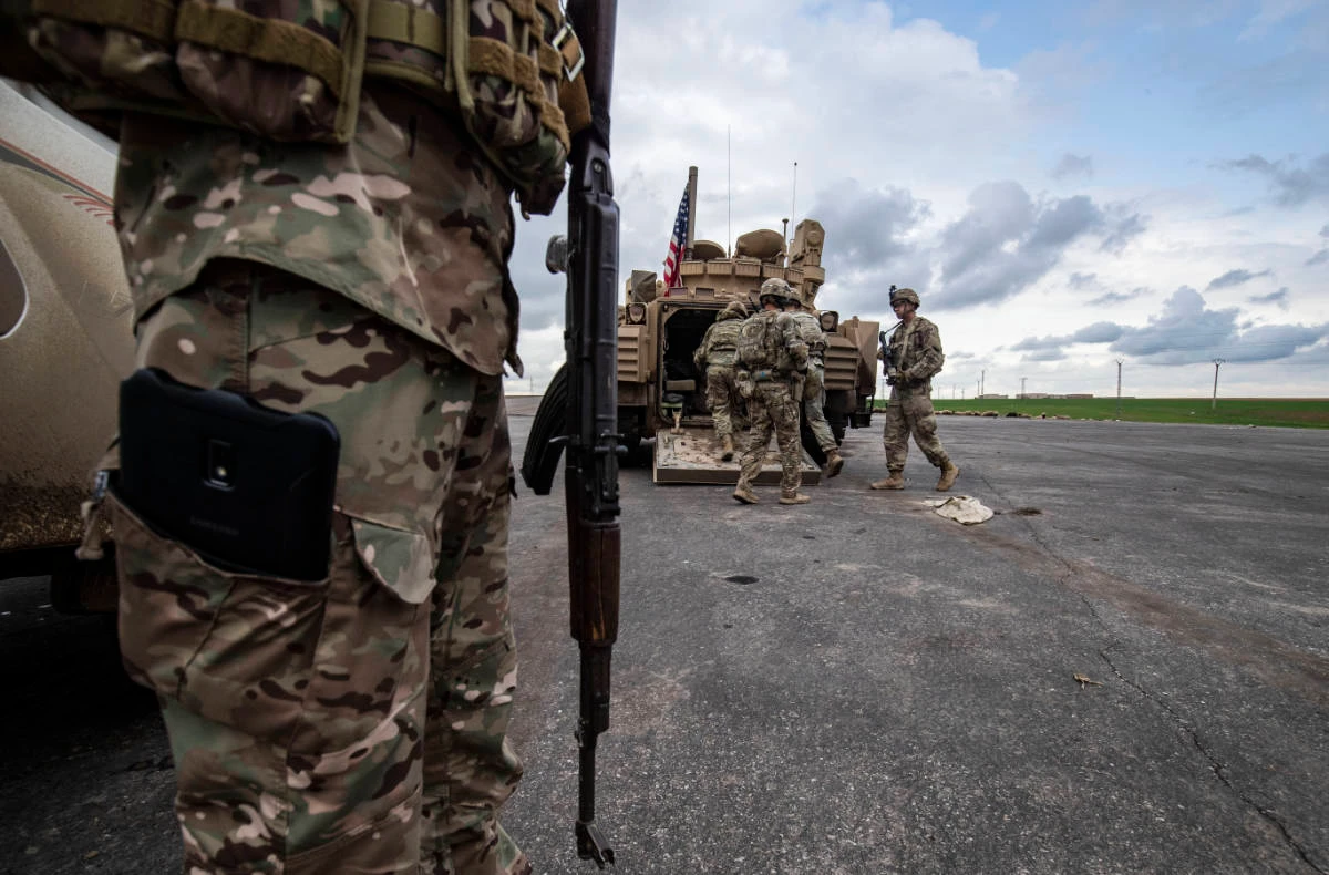A member of the Syrian Democratic Forces (SDF) (L) and US soldiers are pictured near an armoured military vehicles are pictured on the outskirts of Rumaylan in Syria's northeastern Hasakeh province, bordering Turkey, on March 27, 2023. (AFP)