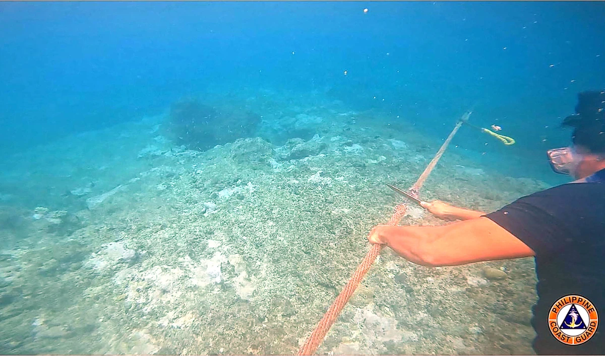 A coast guard diver cuts a rope attached to a floating barrier blocking the entrance to Scarborough shoal in the disputed South China sea. (AFP)
