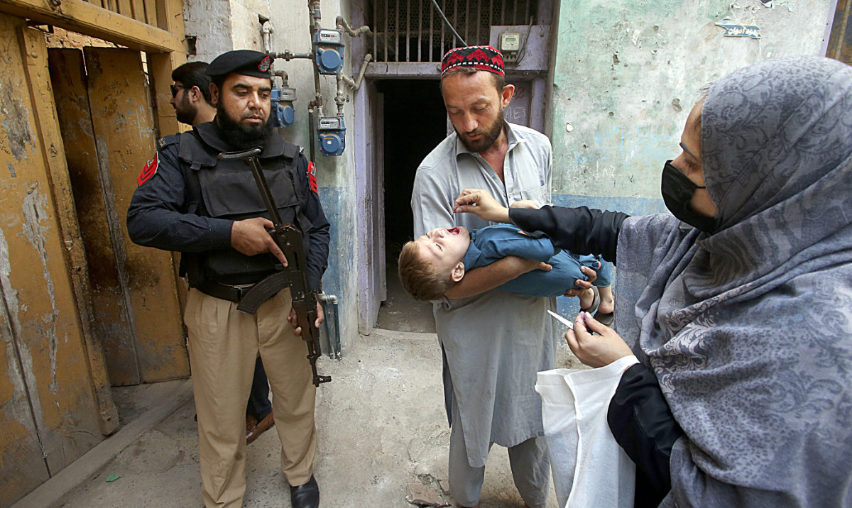 A police officer stands guard as a health worker administers a polio vaccine to a child at a neighborhood of Peshawar, Pakistan, Monday. (AP)