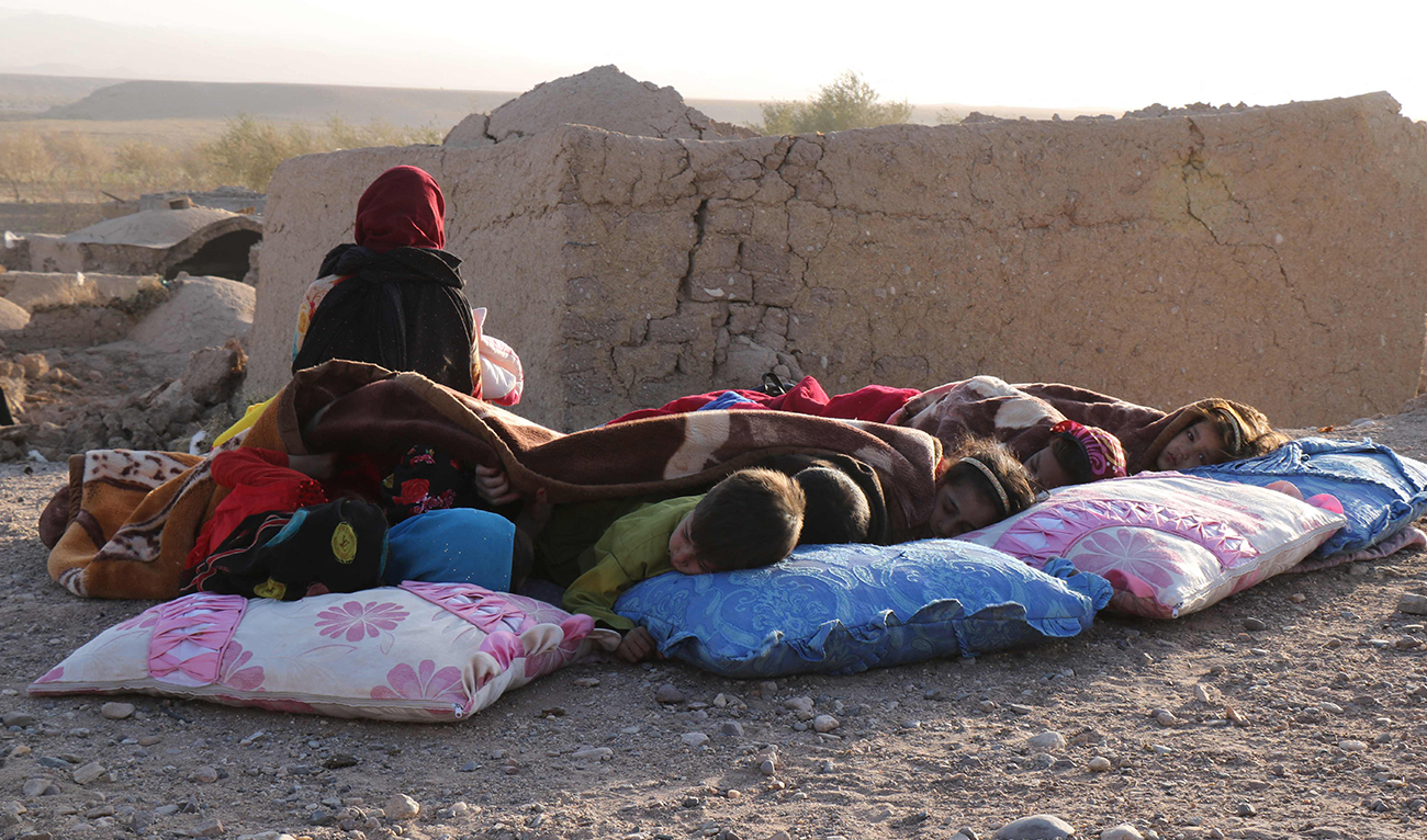 Afghan children rest under a blanket beside damaged houses after earthquake in Sarbuland village of Zendeh Jan district of Herat province on October 7,2023. (AFP)