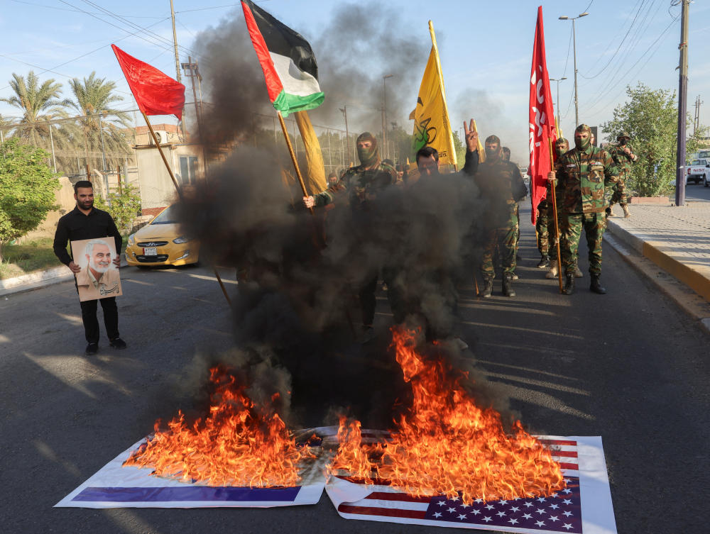 US and Israeli national flags burn, as members of Harakat Hezbollah al Nujaba, gather next to fire during a protest in solidarity with Palestinians in Gaza, in Baghdad. (Reuters)