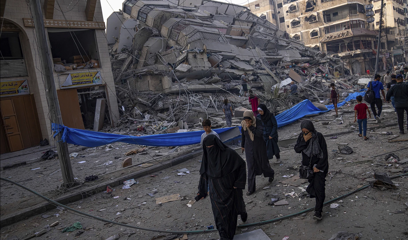 Palestinians walk by the rubble of a building after it was struck by an Israeli airstrike in Gaza city on October 8, 2023. (AP)