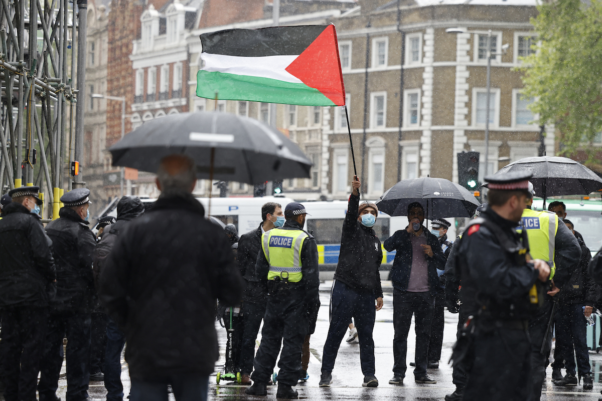 A pro-Palestinian protester with a Palestinian flag is seen behind a police cordon outside the Israeli Embassy in London. (File/AFP)