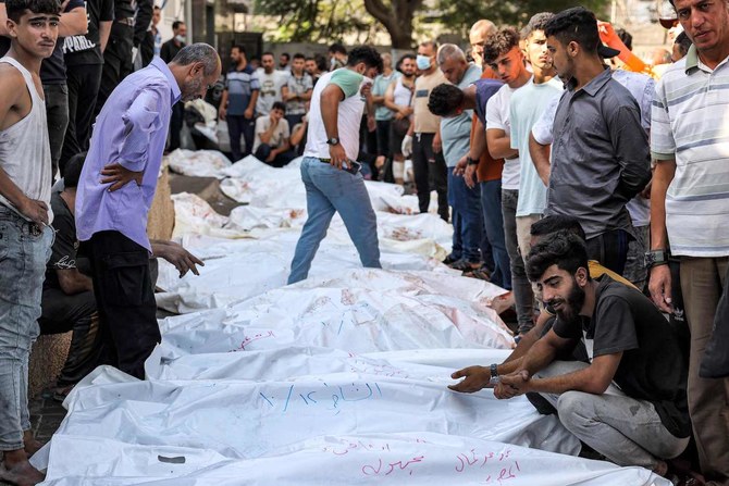 People stand by the bodies of victims of Israeli air strikes outside the morgue of Al-Shifa hospital in Gaza City on October 12, 2023. (AFP)