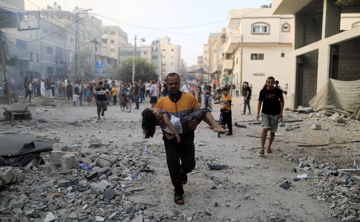 A Palestinian carrying achild runs following an Israeli strike, in Khan Yunis in the southern Gaza Strip on October 14, 2023. (File/AFP)