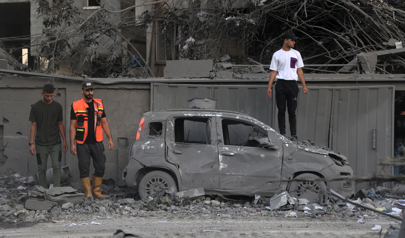 A rescuer and people stand near a burnt car following an Israeli strike in Rafah in the southern Gaza Strip, on October 15, 2023. (AFP)