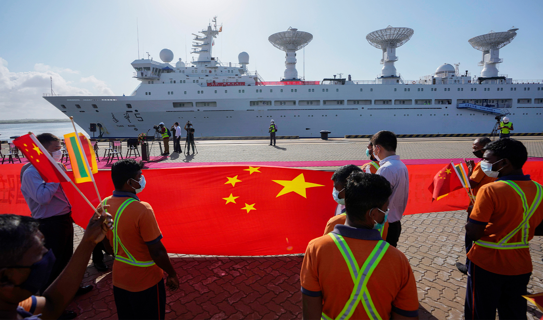 Sri Lankan port workers hold a Chinese national flag to welcome Chinese research ship Yuan Wang 5, bristling with surveillance equipment, as it arrives in Hambantota International Port in Hambantota, Sri Lanka, on August 16, 2022. (AP/File)