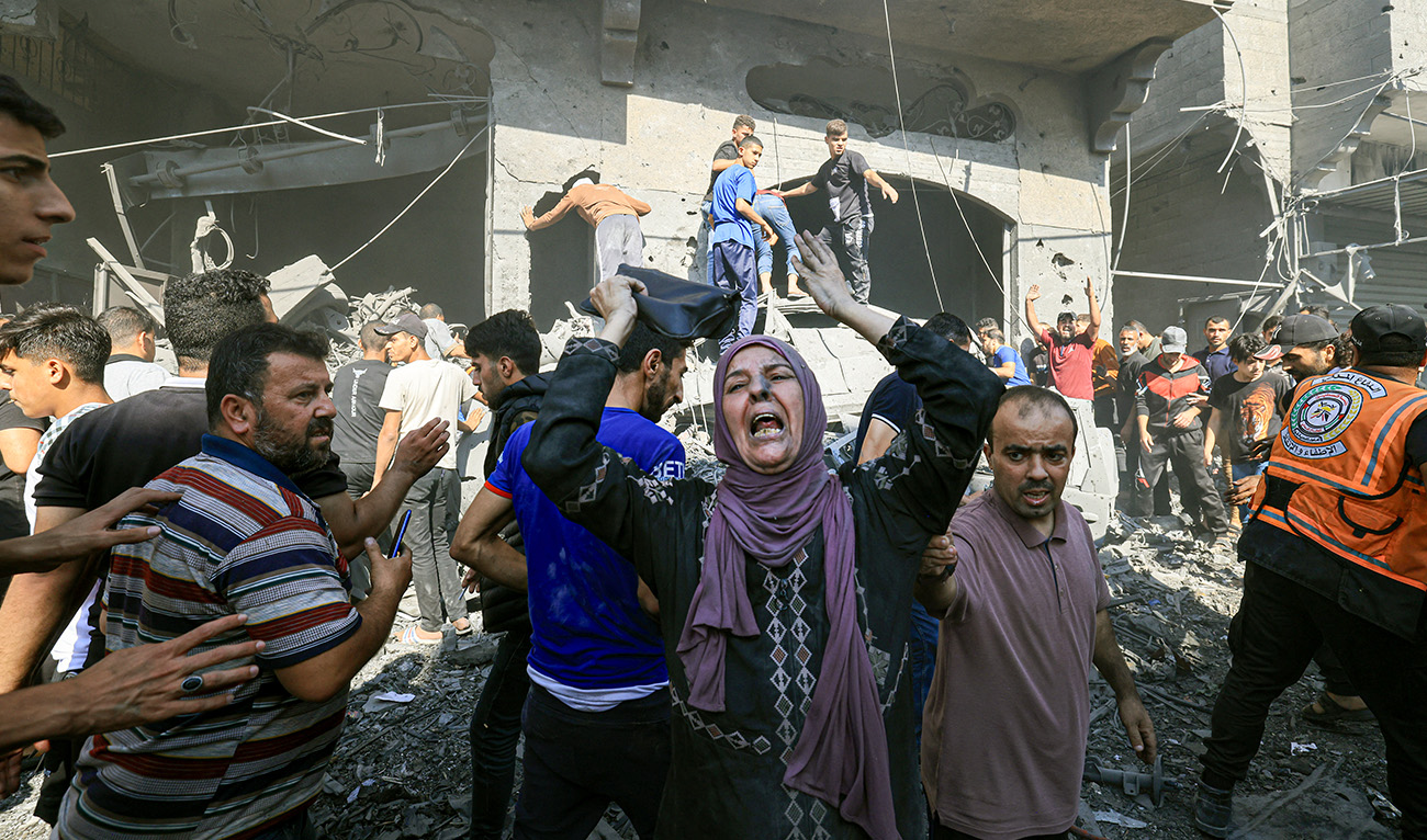 A Palestinian woman reacts as others rush to look for victims in the rubble of a building following an Israeli strike in Khan Yunis in the southern Gaza Strip on October 17, 2023. (AFP)
