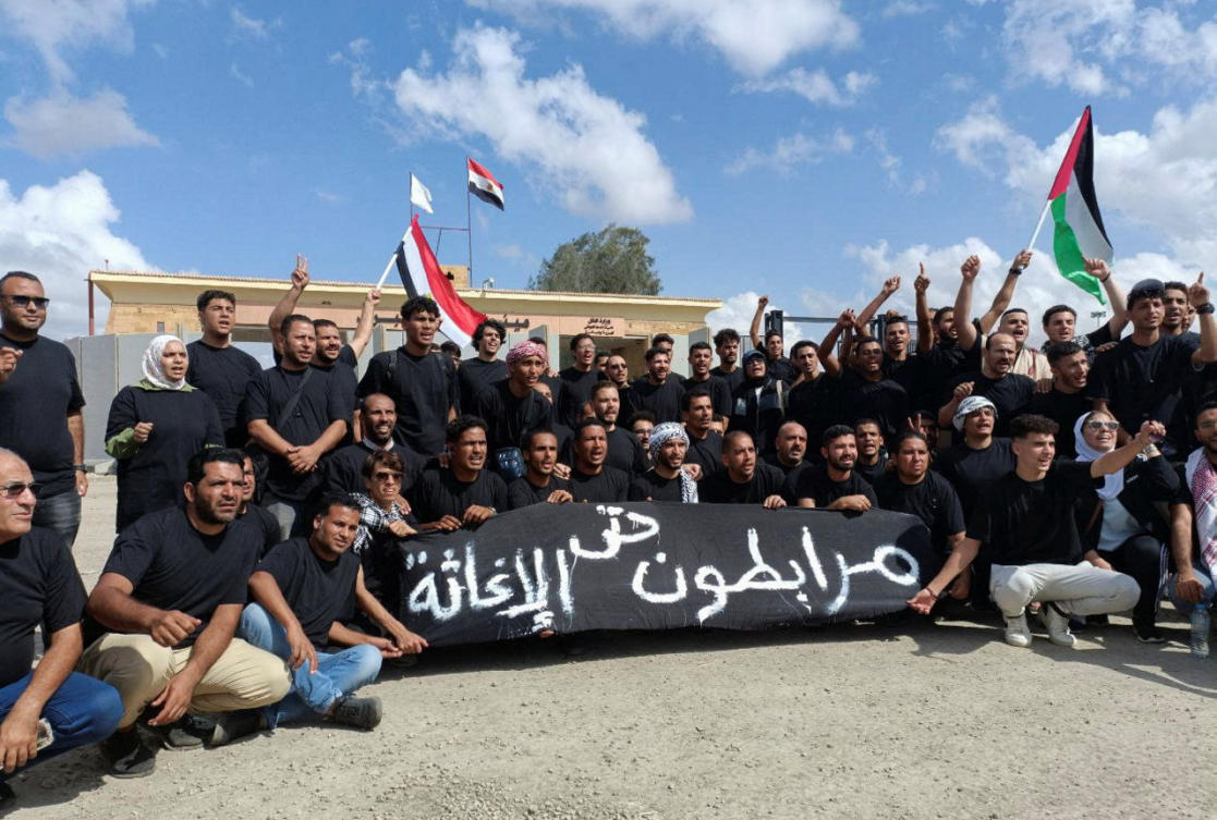 Egyptian volunteers shout slogans, with a banner that reads “Standing solid until relief,” in front of the Rafah crossing, as trucks carrying humanitarian aid for Palestinians await a decision for it to open to enter Gaza in Rafah, Oct. 18, 2023. (Reuters)