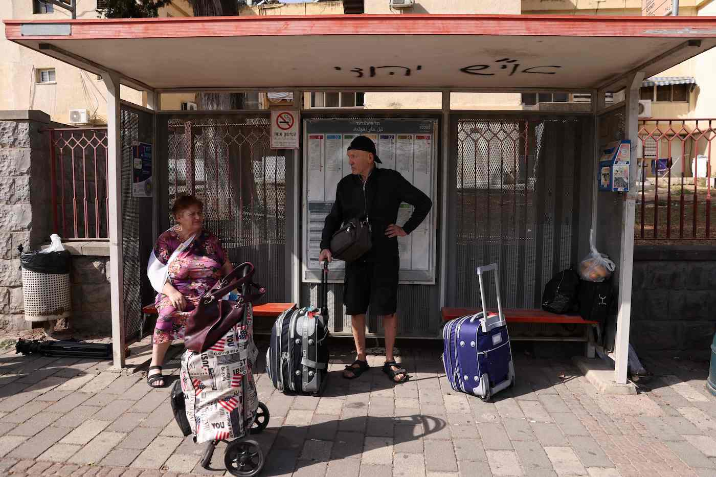 People with their luggage wait at a bus stop in the northern Israeli town of Kiryat Shmona on the border with Lebanon, to be evacuated on Oct. 22, 2023. (AFP)
