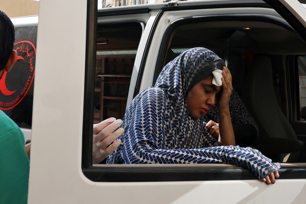 A young woman holds a handkerchief to her forehead as she leans against the window of an ambulance outside a hospital following an Israeli strike in Rafah in the southern Gaza Strip on Oct. 22, 2023. (AFP)