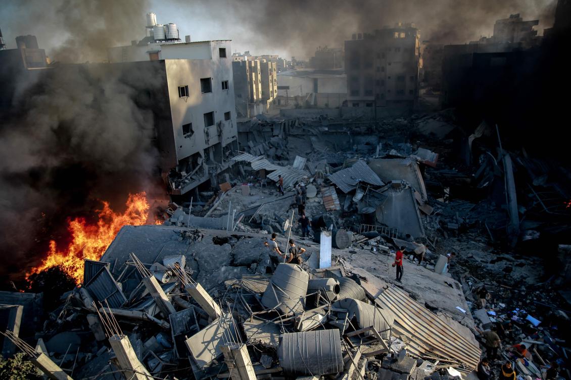 Smoke and fire rise from a levelled building as people gather amid the destruction in the aftermath of an Israeli strike on Gaza City on October 26, 2023, as battles continue between Israel and the Palestinian Hamas group. (AFP)