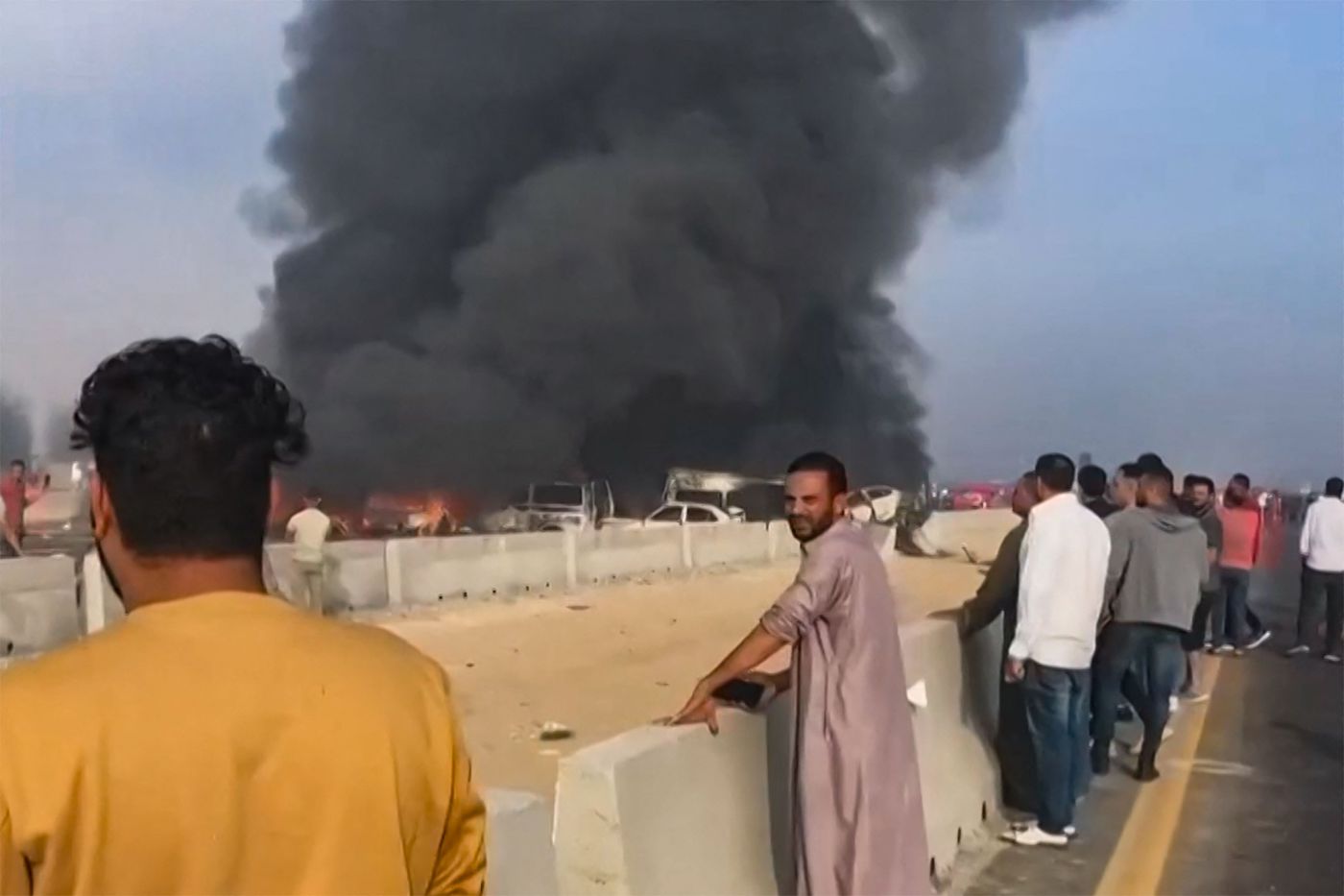 People watch as black smoke billows from charred vehicles following a collision on the Cairo-Alexandria desert road near Wadi Al-Natrun. (AFP)