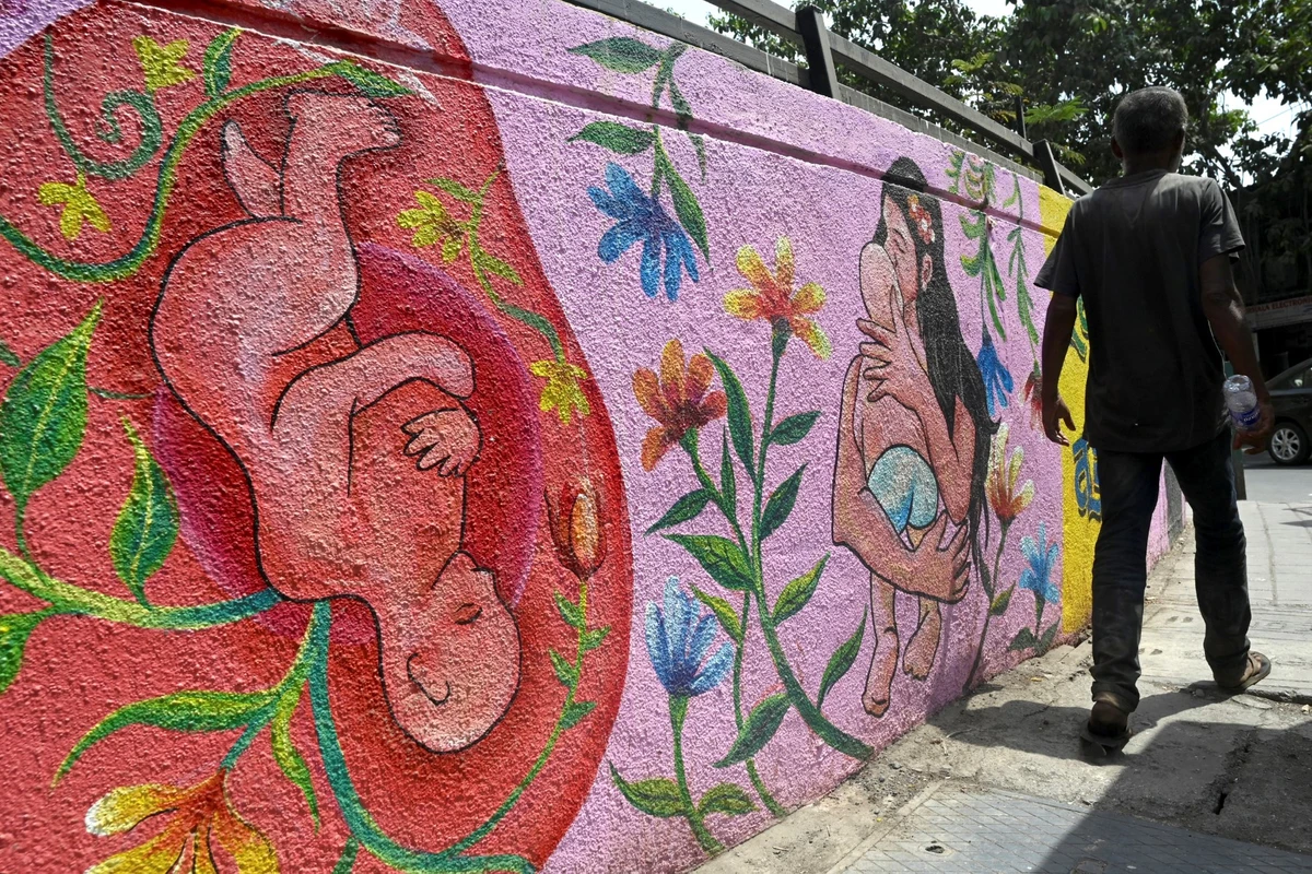 A man walks past a wall mural of a mother cradling her newborn baby in Mumbai, India, on May 8, 2022. (AFP)