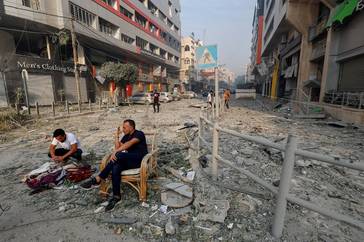 Palestinians sit on a debris-strewn street near the Watan Tower, which was destroyed in Israeli strikes, in Gaza City on Oct. 8, 2023. (Reuters)