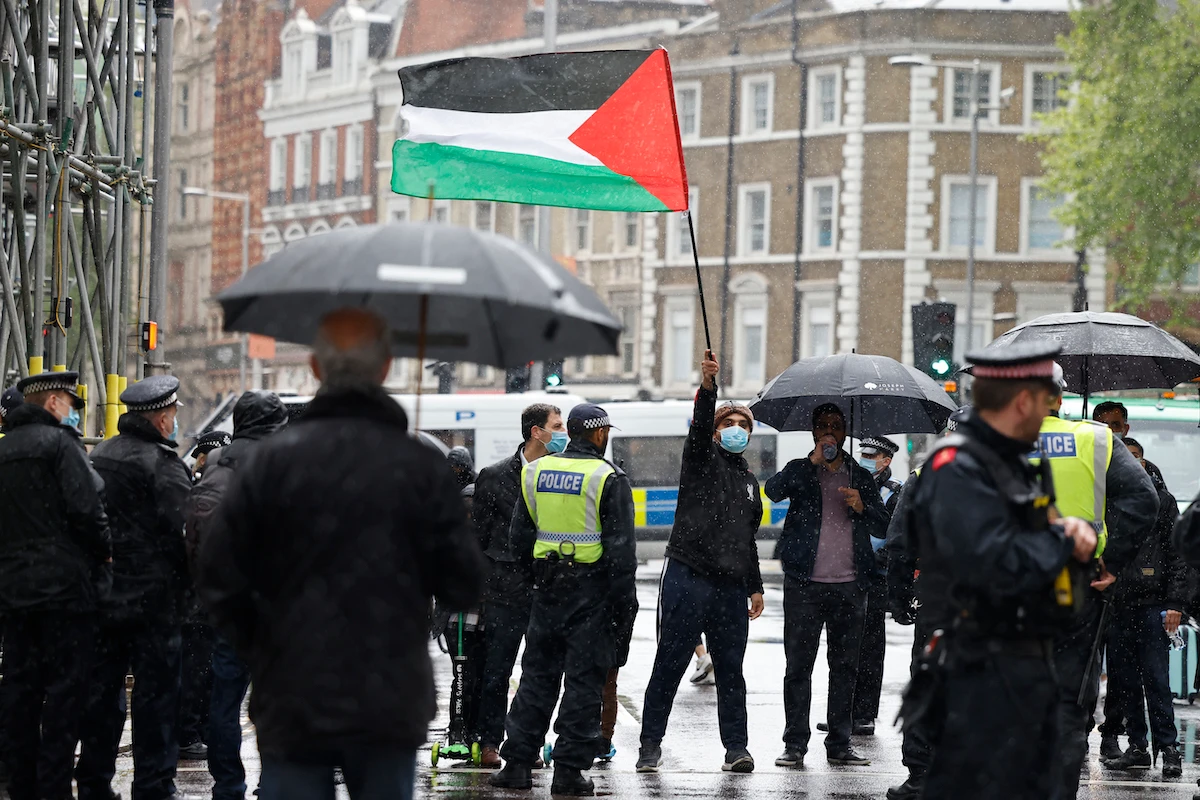 A pro-Palestinian protester with a Palestinian flag is seen behind a police cordon outside the Israeli Embassy in London. (File/AFP)