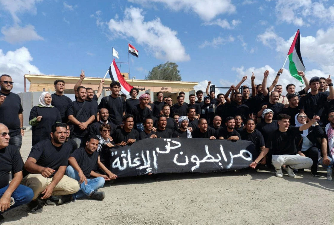 Egyptian volunteers shout slogans, with a banner that reads “Standing solid until relief,” in front of the Rafah crossing, as trucks carrying humanitarian aid for Palestinians await a decision for it to open to enter Gaza in Rafah, Oct. 18, 2023. (Reuters)