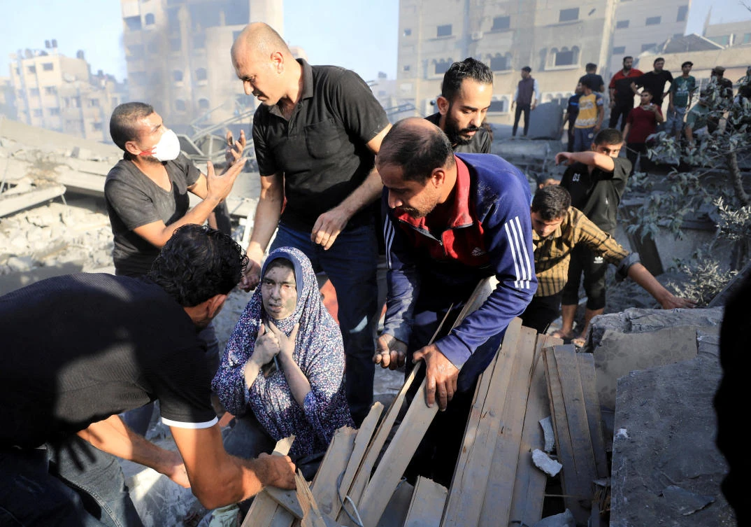 A Palestinian woman is assisted, as people search for casualties at the site of an Israeli strike on a residential building in Gaza City, October 25, 2023. (Reuters)