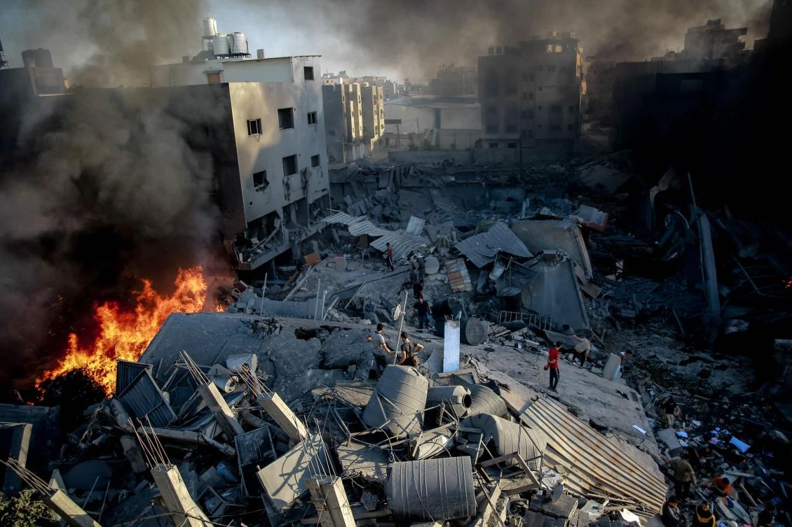 Smoke and fire rise from a levelled building as people gather amid the destruction in the aftermath of an Israeli strike on Gaza City on October 26, 2023, as battles continue between Israel and the Palestinian Hamas group. (AFP)