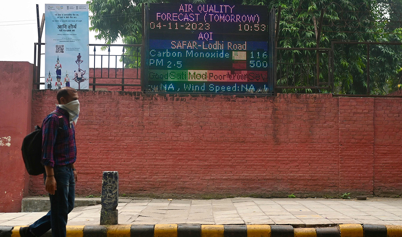 A man wearing a handkerchief as a facemask walks past a display with air quality information amid heavy smog conditions in New Delhi on November 3, 2023. (AFP)