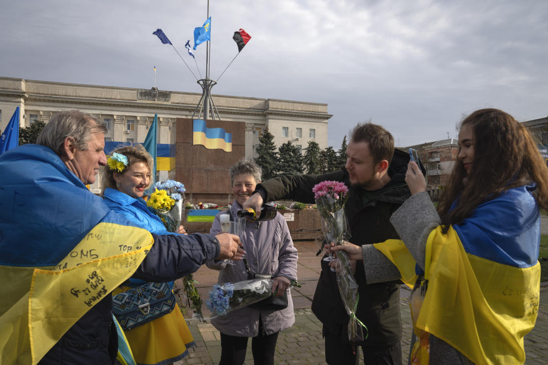 City residents wrapped in the national flags drink champagne and hold flowers as they mark one year since Ukraine retook the city of Kherson from occupying Russian forces, in central square in Kherson, on Nov. 11, 2023. (AP)
