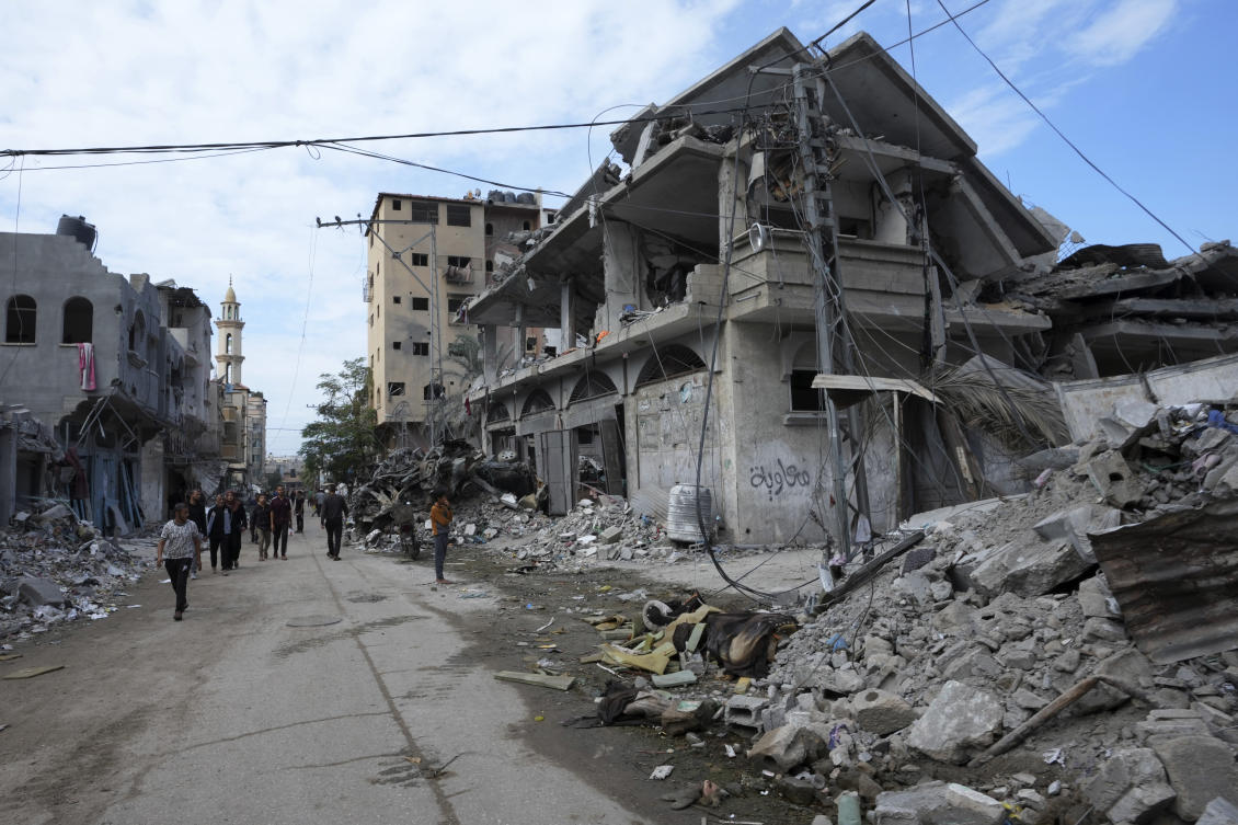Palestinians walk past the buildings destroyed in the Israeli bombardment of the Gaza Strip, at the main road in Bureij refugee camp, Gaza Strip, on Nov. 14, 2023. (AP)
