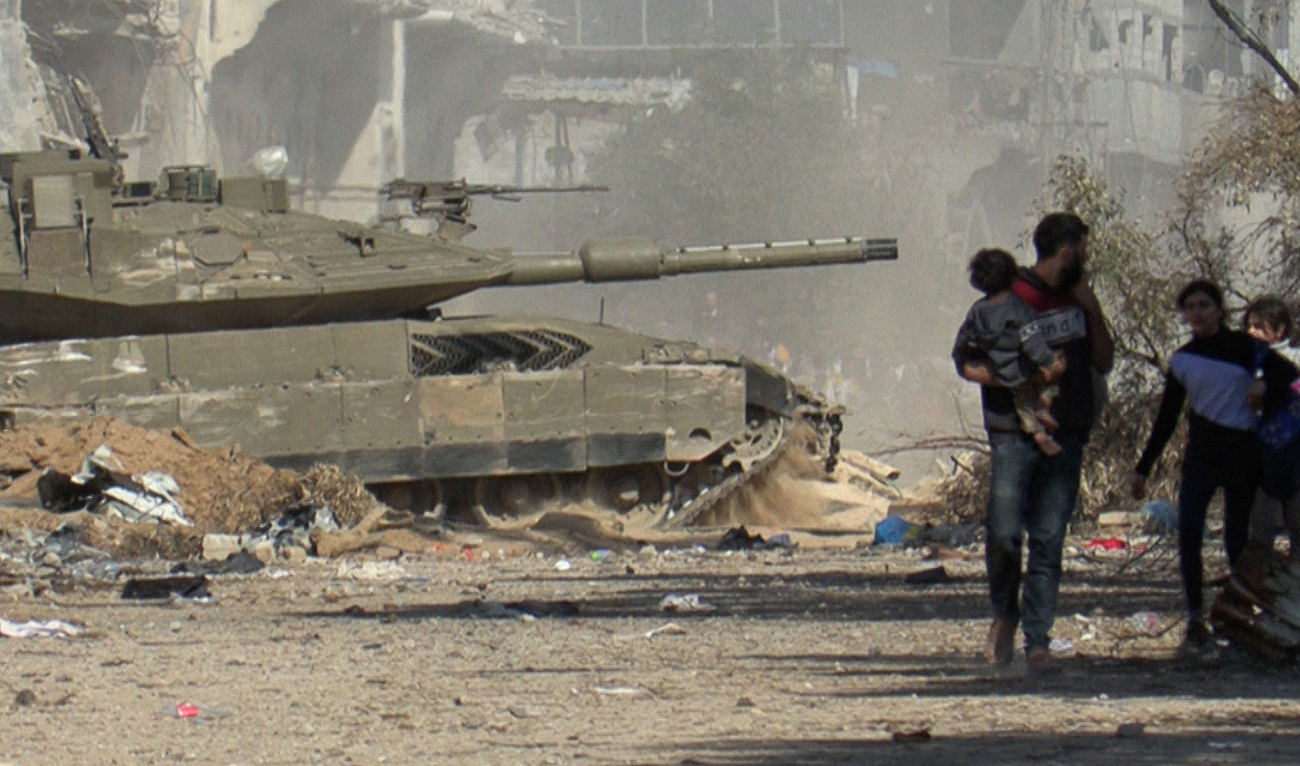 A grab from an AFPTV video shows an Israeli armoured vehicle rolling past Palestinians fleeing Gaza City on foot amid ongoing battles between Israel and the Palestinian Hamas movement on November 18, 2023. (AFP)
