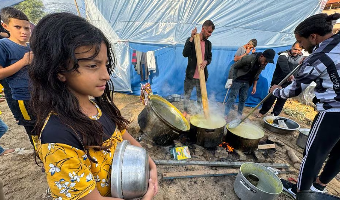 Children wait while displaced Palestinians, who fled their houses due to Israeli strikes, cook lentil soup on a rainy day at Nasser Hospital in Khan Younis in the southern Gaza Strip on November 20, 2023. (REUTERS)